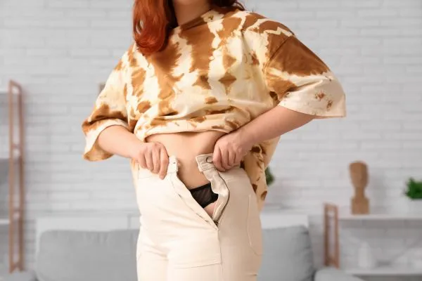 Image of woman trying to do her trousers up after pregnancy weight gain Leeds